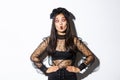 Image of funny asian girl celebrating halloween, wearing gothic lace dress to impersonate witch, showing silly faces and