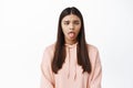 Image of funny young woman making sad face, squinting and showing tongue from something disgusting, standing in hoodie