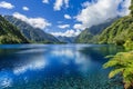 Tranquil blue lake with clear sky and white clouds above, encircled by lush greenery and towering mountains, promoting serenity Royalty Free Stock Photo