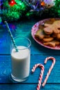 Image of ginger biscuits, glass of milk, caramel sticks, spruce branches with burning garland