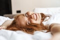 Image of ginger happy woman smiling at camera while lying in bed