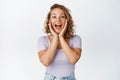 Image of girl touched her face and screams from amazement, receive surprise news, standing against white background