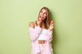 Image of glamour blond girl in pink outfit, eating macaroons and looking at upper left corner thoughtful, standing over Royalty Free Stock Photo