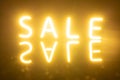 Image of glowing neon sale text with reflection over orange background