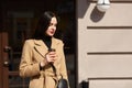 Image of gorgeous brunette woman with long hair, wearing coat and black handbag, has bright red manicure, holding takeaway coffee Royalty Free Stock Photo