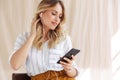 Image of gorgeous elegant blonde woman in earphones holding smartphone