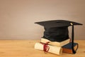 Image of graduation black hat over old books next to graduation on wooden desk. Education and back to school concept. Royalty Free Stock Photo