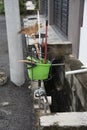 Green plastic pail of unwanted household cleaning objects by the street.