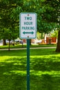 Green Two Hour Parking sign in front of park in summertime