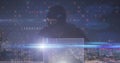 Image of hacker in balaklava using laptop with cyberattack text over cityscape