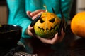 Image of hands holding jack-o-lantern from pumpkin sitting at wooden table Royalty Free Stock Photo