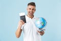 Handsome excited happy adult man posing isolated over blue wall background holding passport with tickets and globe Royalty Free Stock Photo