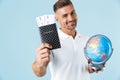 Handsome excited happy adult man posing isolated over blue wall background holding passport with tickets and globe Royalty Free Stock Photo