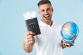 Handsome excited happy adult man posing isolated over blue wall background holding passport with tickets and globe Royalty Free Stock Photo