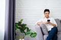 Image of handsome joyful man smiling and working with smartphone while sitting on sofa at home Royalty Free Stock Photo