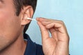 Image of handsome man standing over blue wall background holding cotton bud take care of his ears cleaning it Royalty Free Stock Photo