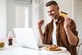 Image of smiling man making winner gesture and holding credit card