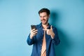 Image of handsome smiling man reading mobile screen and pointing at phone, checking out online promo or smartphone app