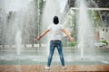 Image of handsome young bearded thoughtful man in summer clothes standing in front of beautifull fountain.