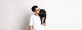 Image of handsome young man kissing his cute black pug, holding dog on shoulder, standing over white background Royalty Free Stock Photo