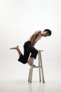 Image of handsome young man posing shirtless in black trousers, jumping on high chair against white studio background Royalty Free Stock Photo