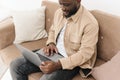Image of happy afro american man working on laptop, watching social media news or doing online shopping while sitting in Royalty Free Stock Photo