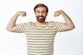 Image of happy bearded guy shows his muscles, flexing biceps on arms and smiling, workout results, feeling strong
