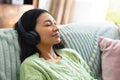 Image of happy biracial woman in headphones relaxing on sofa with eyes closed at home, copy space Royalty Free Stock Photo