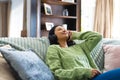 Image of happy biracial woman in headphones, relaxing on sofa with eyes closed at home, copy space Royalty Free Stock Photo
