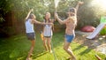 Photo of happy cheerful girls in wet clothes dancing and jumping under water garden hose. Family playing and having fun Royalty Free Stock Photo