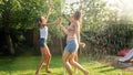 Photo of happy cheerful girls in wet clothes dancing and jumping under water garden hose. Family playing and having fun Royalty Free Stock Photo