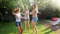 Photo of happy cheerful girls in wet clothes dancing and jumping under water garden hose. Family playing and having fun Royalty Free Stock Photo