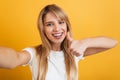 Happy positive pleased young blonde woman posing isolated over yellow wall background dressed in white casual t-shirt take selfie Royalty Free Stock Photo