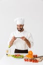 Image of happy cook man in uniform smiling and taking photo of plate with vegetable salad on smartphone