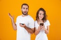 Image of happy couple man and woman smiling while both using mobile phones, isolated over yellow background Royalty Free Stock Photo