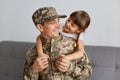 Image of happy delighted man soldier wearing camouflage uniform and cap, posing with his daughter, hugging each other, male came Royalty Free Stock Photo