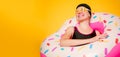 Image of happy girl in swimming goggles, swimsuit with donut life buoy on empty orange background
