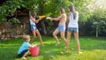 Photo of happy laughing family splashing water with water guns and garden hose at backyard. People playing and having Royalty Free Stock Photo