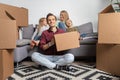 Image of happy man sitting on floor and women with boy and girl sitting on gray sofa among cardboard boxes Royalty Free Stock Photo