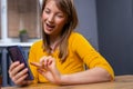 Image of happy nice, blonde, young woman in pajamas, smiling and using cellphone while sitting on the floor in living room Royalty Free Stock Photo