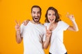 Image of happy people man and woman in basic clothing showing victory sign, while standing together isolated over yellow Royalty Free Stock Photo