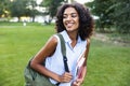 Smiling young african girl on grass outdoors in park holding books looking aside. Royalty Free Stock Photo