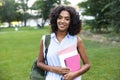 Smiling young african girl on grass outdoors in park holding books looking camera. Royalty Free Stock Photo