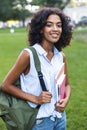 Smiling young african girl on grass outdoors in park holding books looking camera. Royalty Free Stock Photo