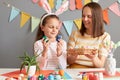 Image of happy woman and daughter wearing bunny ears painting eggs, decorating Easter basket preparing for holiday together Royalty Free Stock Photo