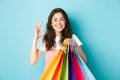 Image of happy young glamour woman shop in stores with discounts, showing okay sign, holding shopping bags, looking Royalty Free Stock Photo