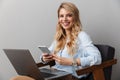 Happy young pretty blonde business woman posing  grey wall background using laptop computer and mobile phone Royalty Free Stock Photo