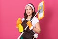 Image of happy young woman holding mop over shoulder and deterjent, maid with cleaning products isolated over pink background, Royalty Free Stock Photo