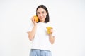 Image of healthy young woman, holds glass of fresh juice and orange fruit, smiles thoughtful, isolated on white Royalty Free Stock Photo