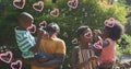 Image of hearts over happy african american family making soap bubbles in garden